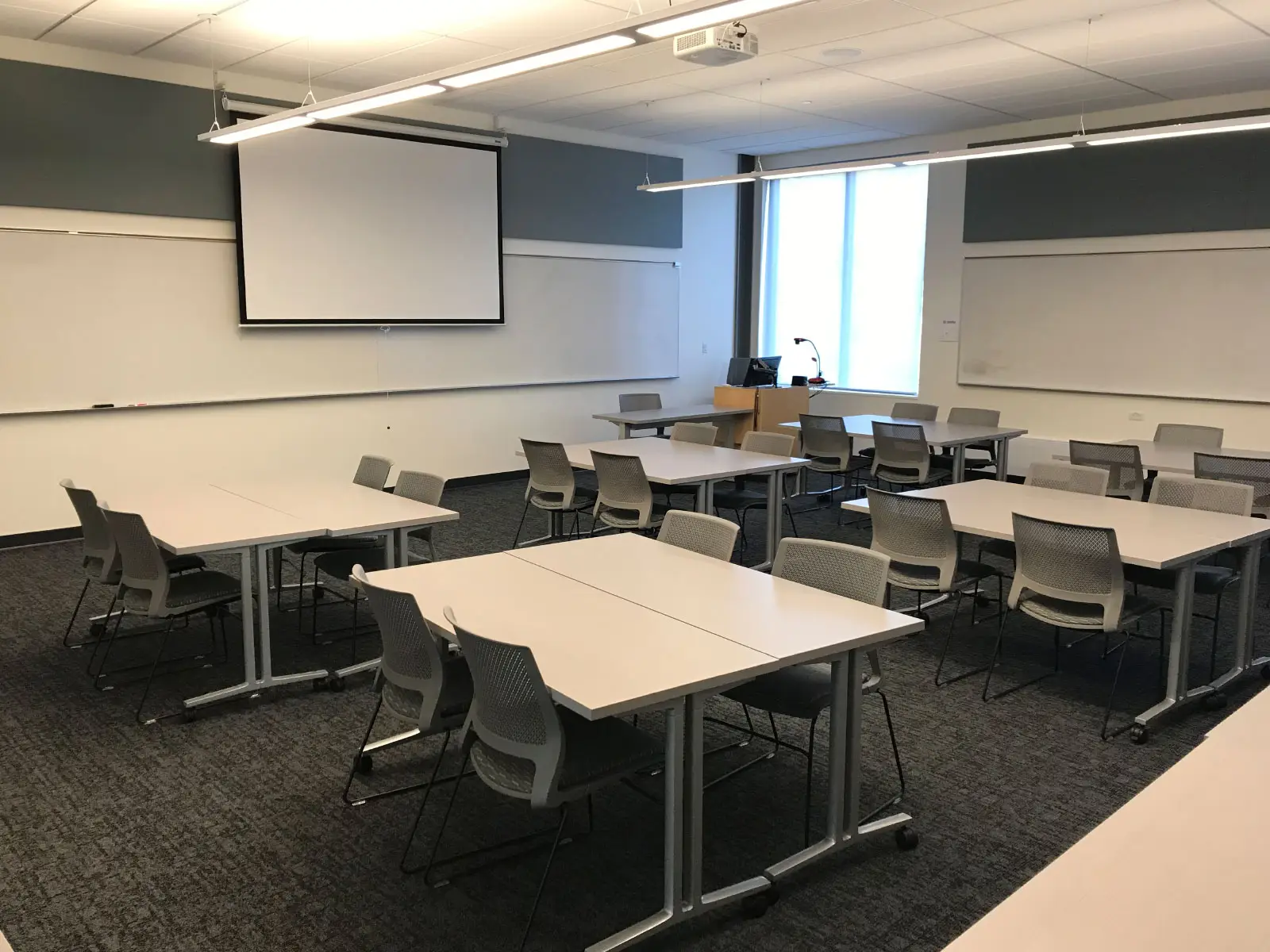 Several tables with chairs in front of a projector screen in a Oregon City campus classroom