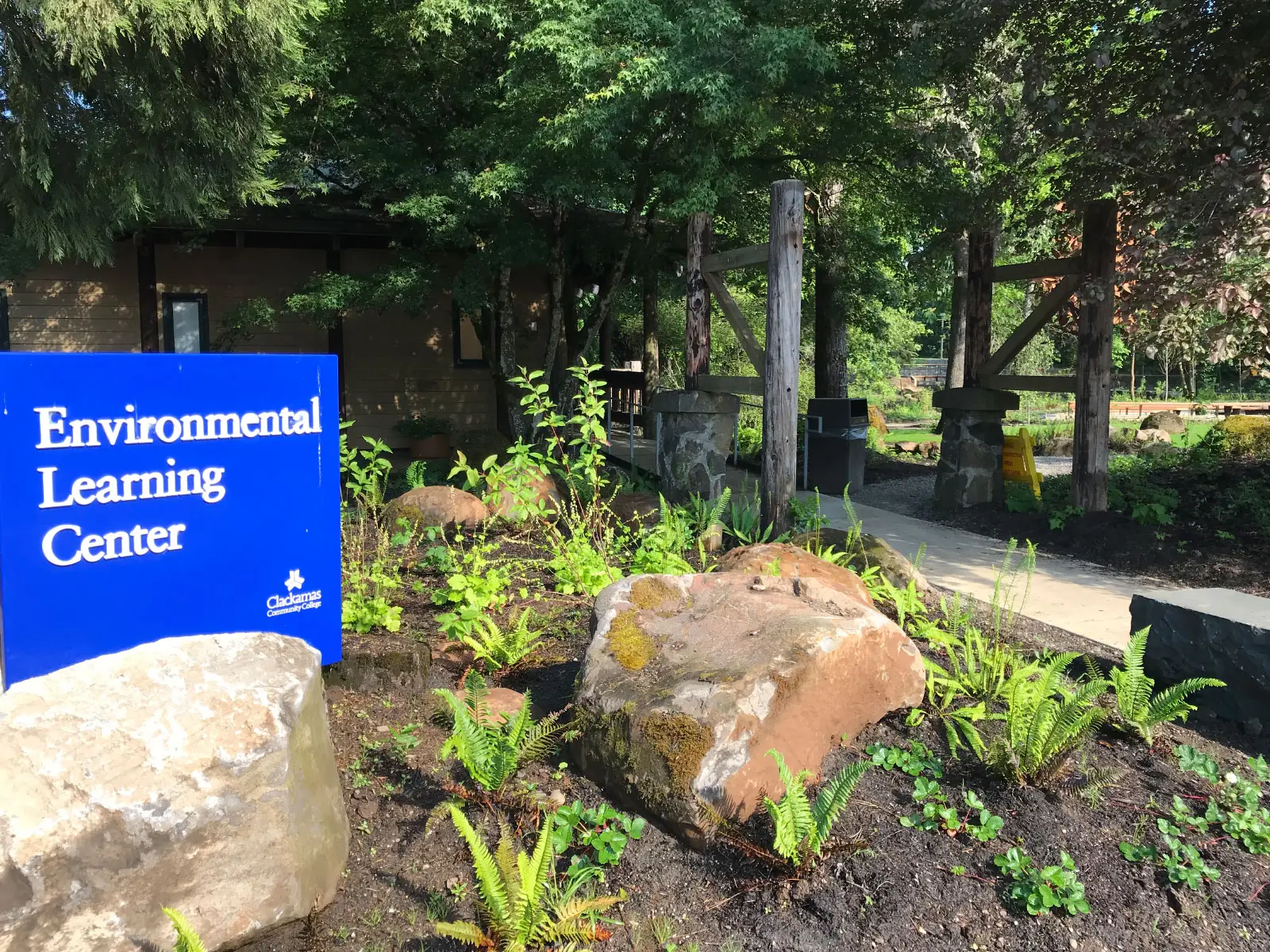 The Environmental Learning Center's blue entrance sign, surrounded by rocks and greenery, just outside Lakeside Hall, at the Oregon City campus