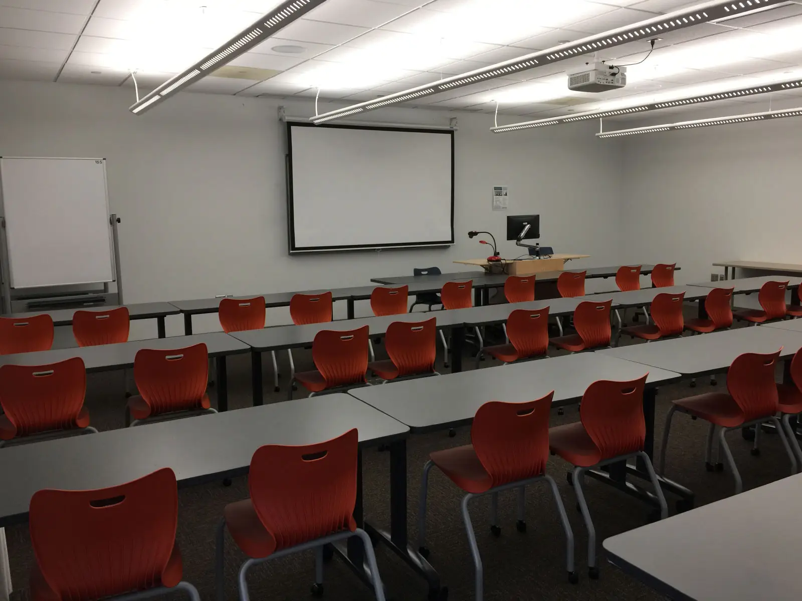Rows of orange chairs and tables in front of a podium and projector in classroom W155 on the WIlsonville campus