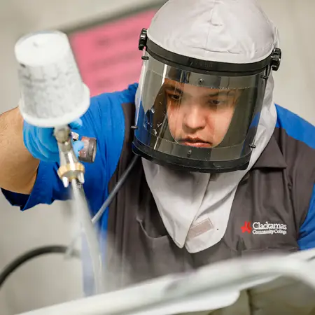 Student wearing protective face shield uses paint sprayer on car