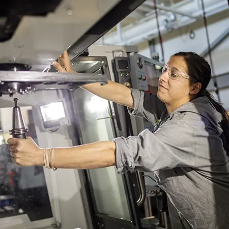 A student in protective eyewear uses industrial technology equipment.