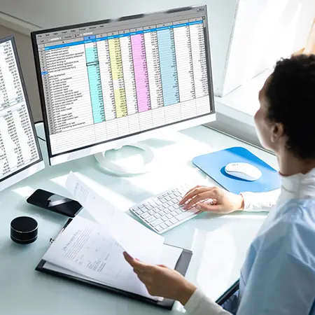 Professional reviews a spreadsheet on computer screens